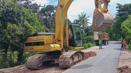 Alat berat excavator terlihat sibuk membongkar ruas jalan yang rusak di Desa Mandeu, Kabupaten Belu.